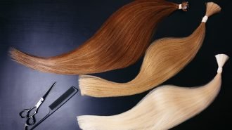 hair extensions of three colors on a dark background with scissors and comb. copyspace. top view